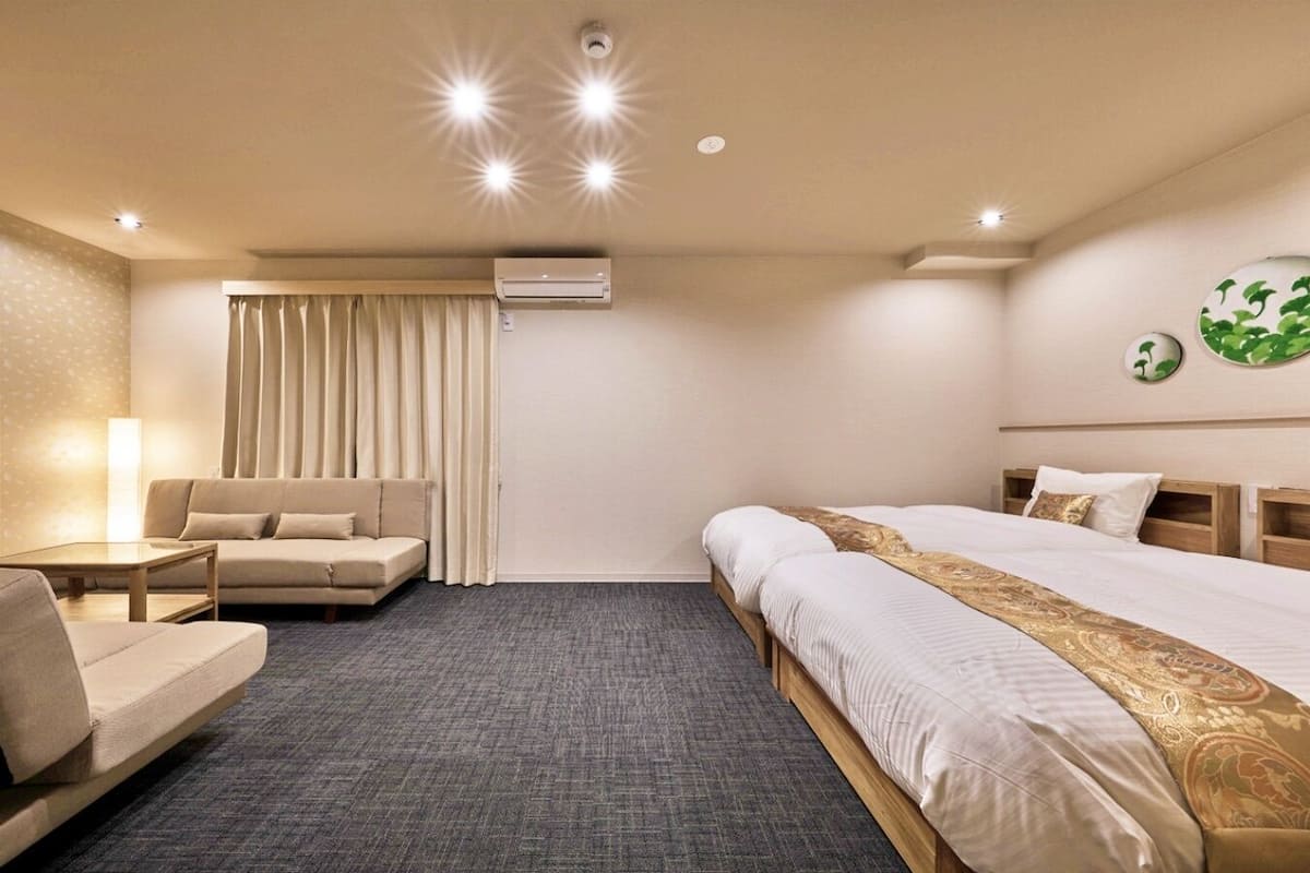 Quarto de hotel com cama, sofá, escrivaninha e janela com cortinas.