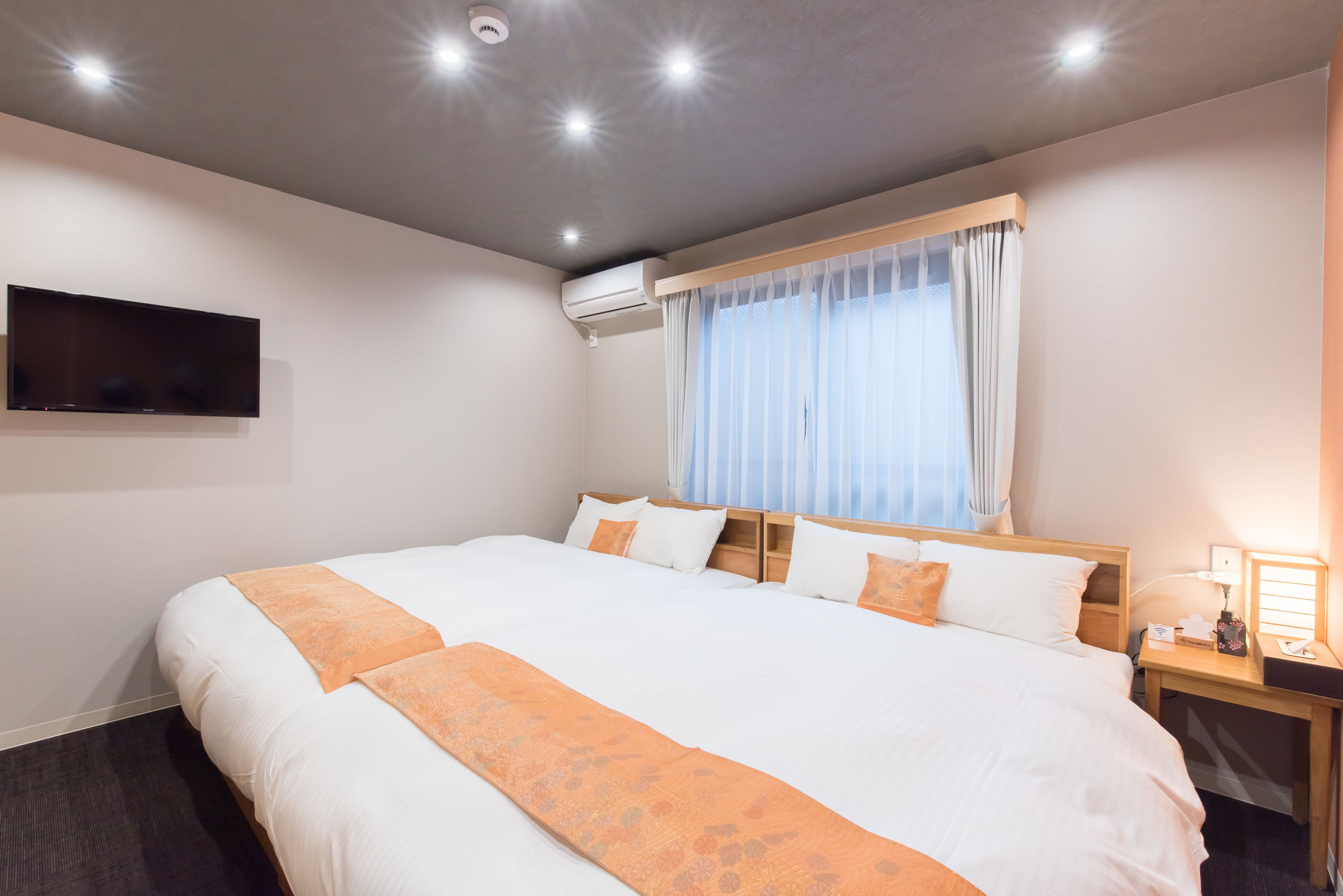Hotelkamer met een groot bed, een flatscreen televisie aan de muur, een airconditioningapparaat, een nachtkastje met een lamp en een raam met gordijnen.
