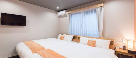 Hotelkamer met een groot bed, een flatscreen televisie aan de muur, een airconditioningapparaat, een nachtkastje met een lamp en een raam met gordijnen.