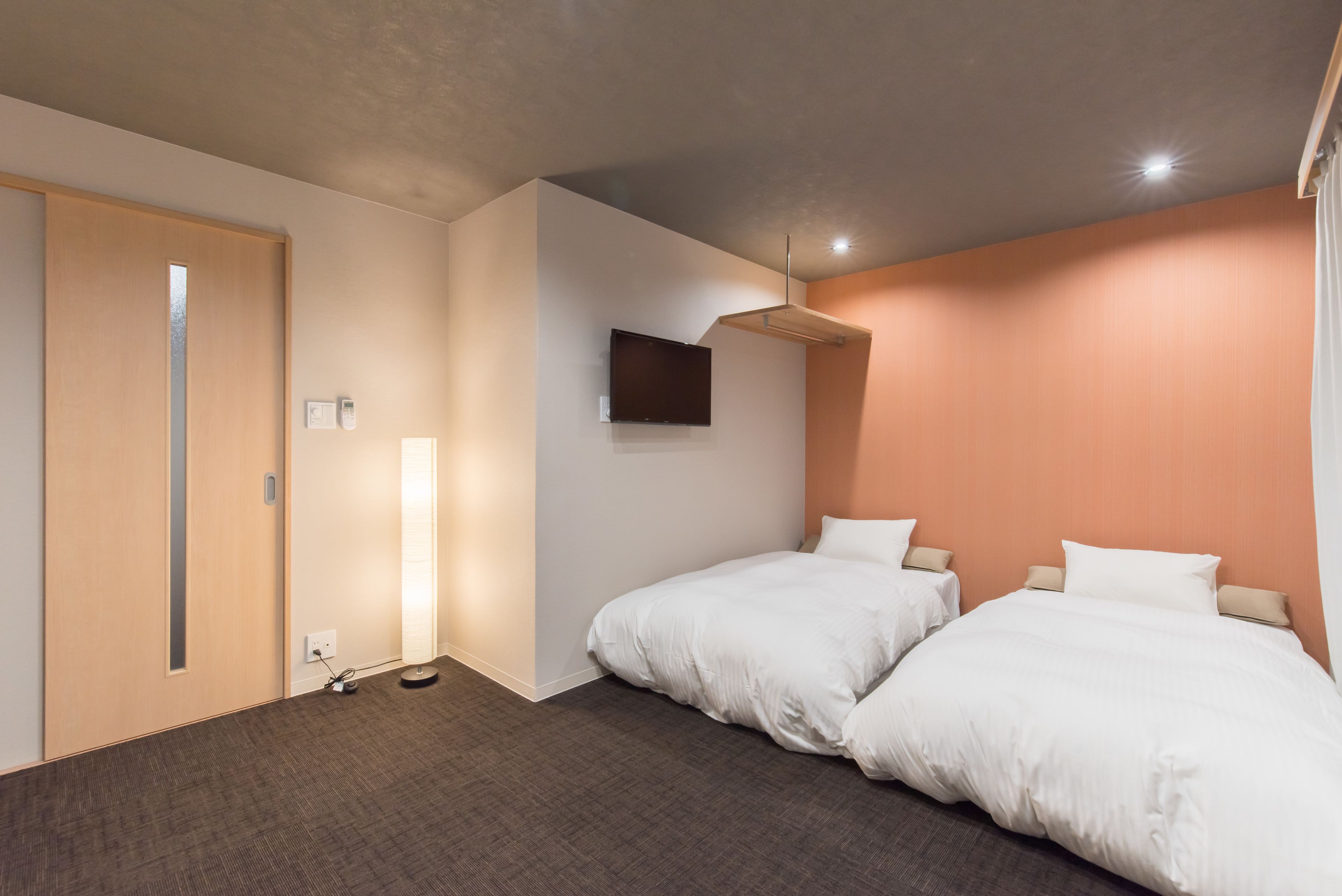 Habitación de hotel con dos camas, un televisor de pantalla plana en la pared, una puerta de madera y piso alfombrado.