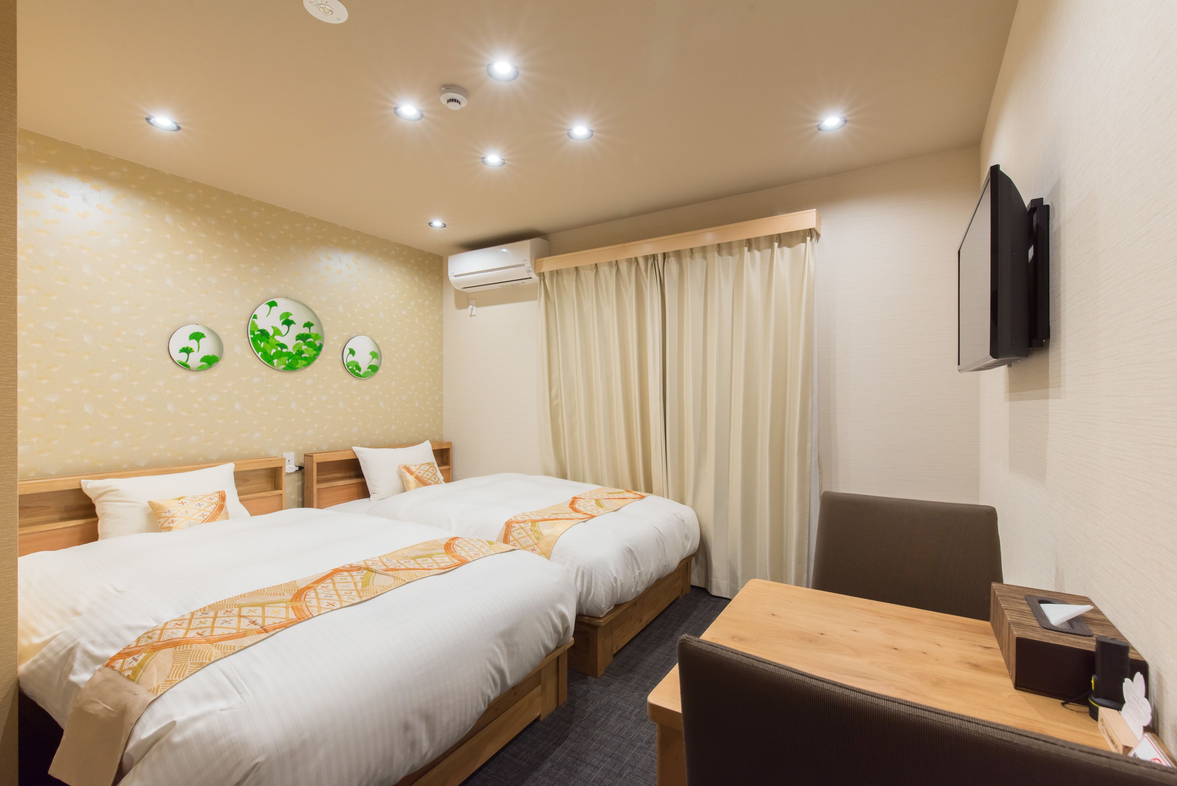 A hotel room with two beds, a wooden desk, a television, and an air conditioning unit.