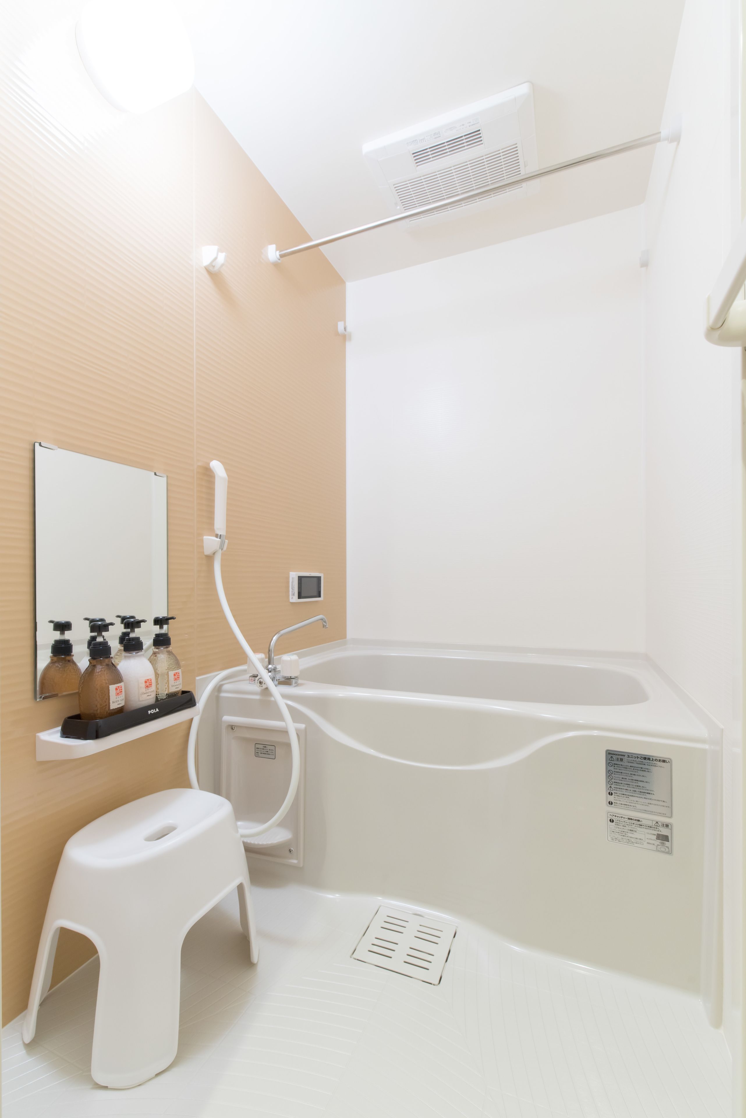 Et badeværelse med badekar, toilet, håndvask og spejl. Der er toiletartikler på håndvasken og en trinbænk ved siden af toilettet.