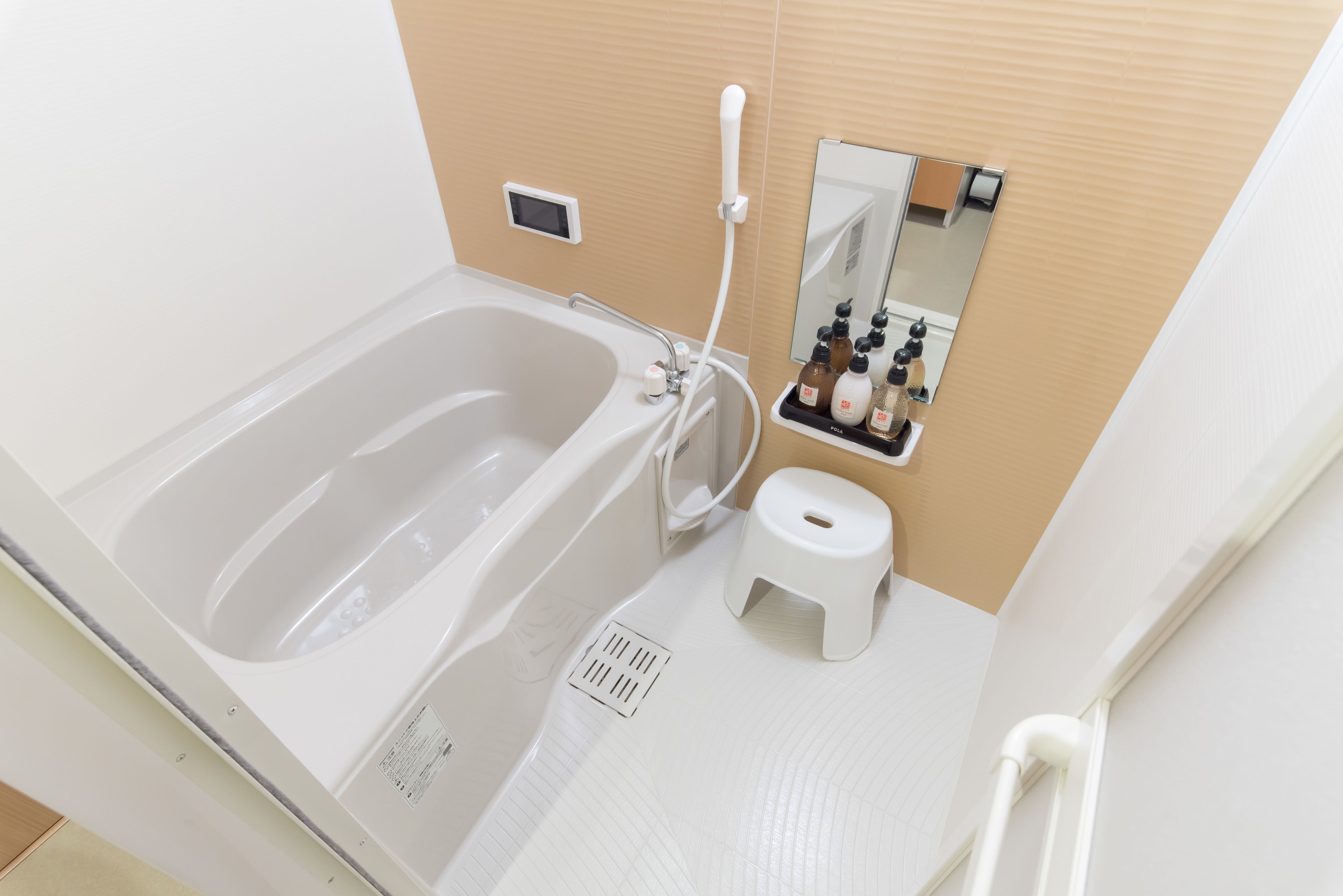 A modern bathroom with a bathtub, a small stool, a shelf with toiletries, and a mirror.