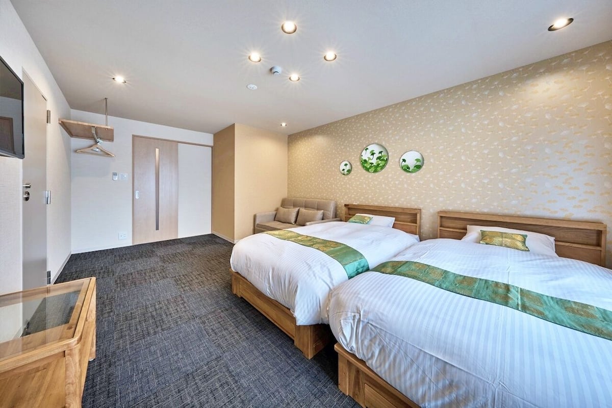 A hotel room with two beds, a wooden headboard, a carpeted floor, a glass table, and a wall-mounted TV.