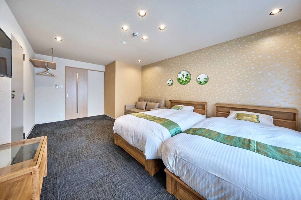 Quarto de hotel com duas camas, cabeceira de madeira, uma mesa pequena e televisão na parede.
