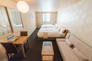 A hotel room with two beds, a sofa, a wooden table, a desk, and a window. - Stay Sakura Kyoto Station South 1 (Kyoto)