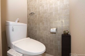 A modern bathroom with a toilet, a wall-mounted toilet paper holder, and a small decorative plant. - Stay Sakura Kyoto Station South 1 (Kyoto)