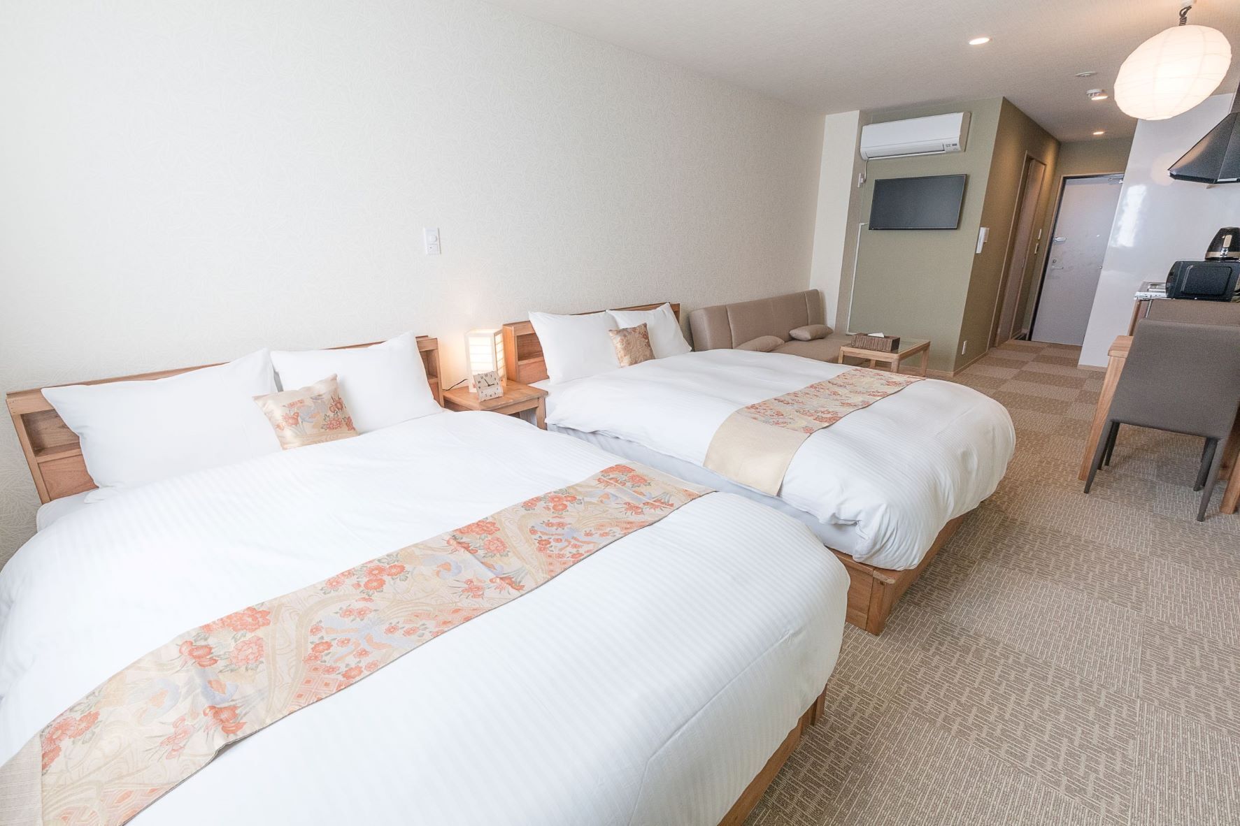 Quarto de hotel com duas camas, uma escrivaninha pequena, uma cadeira e uma televisão.