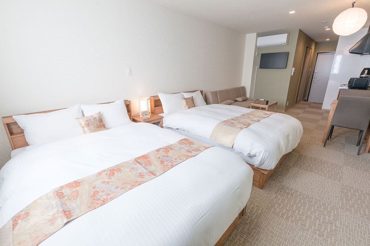 Quarto de hotel com duas camas, uma escrivaninha pequena, uma cadeira e uma televisão.