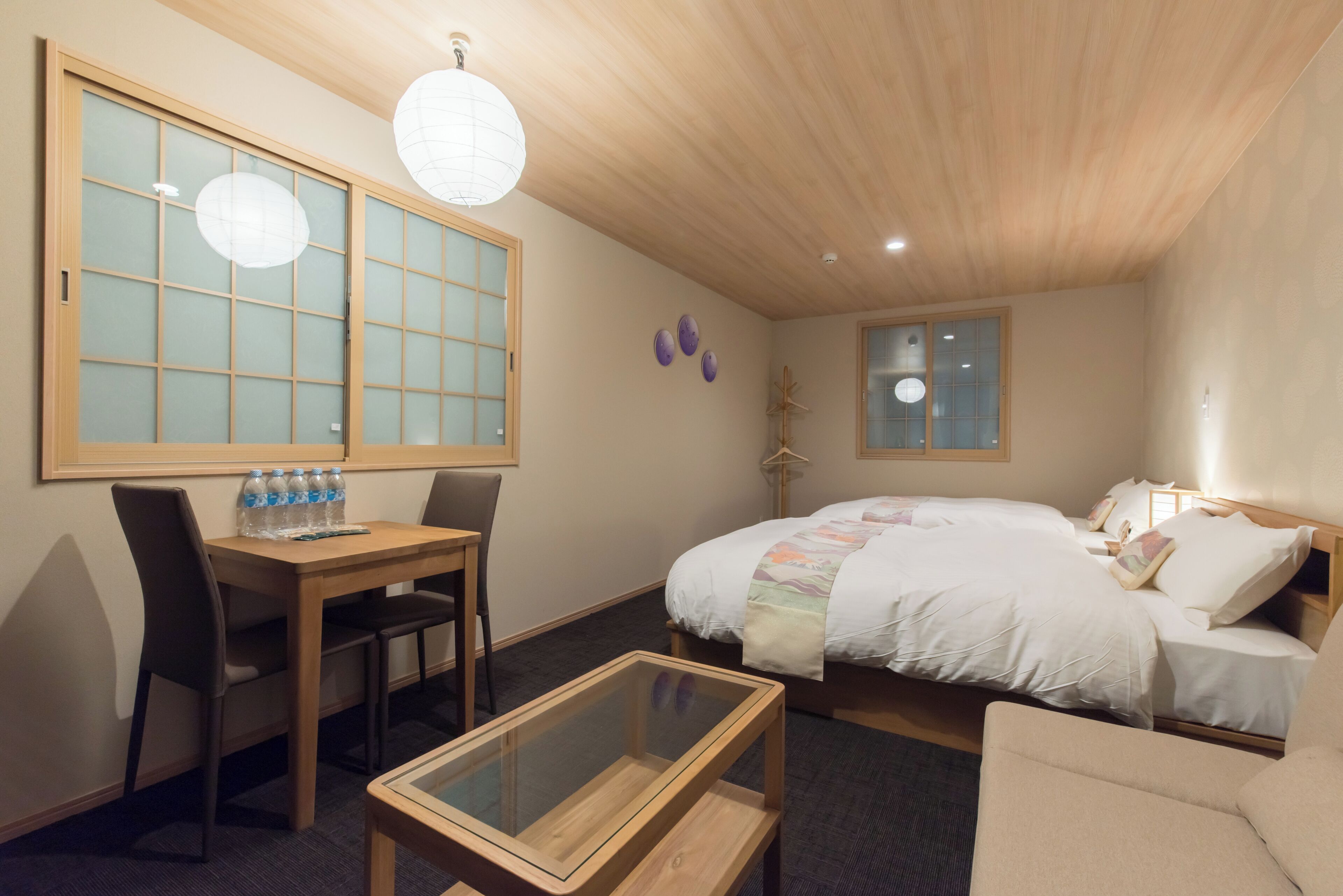 Quarto de hotel com cama, escrivaninha com cadeiras, mesa de vidro e janela com vista.