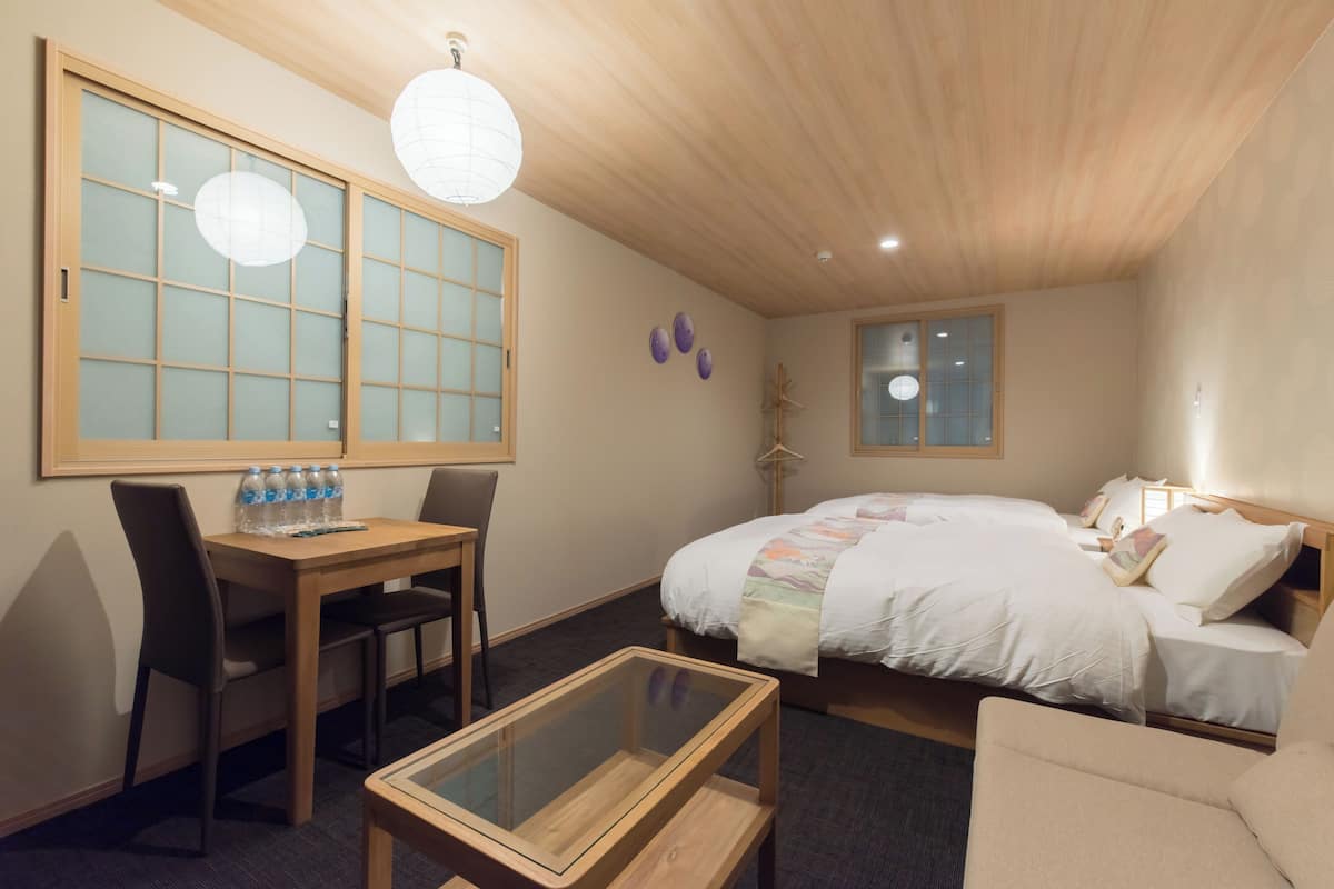 A hotel room with a bed, a desk with chairs, a glass-top table, and a window with a view.
