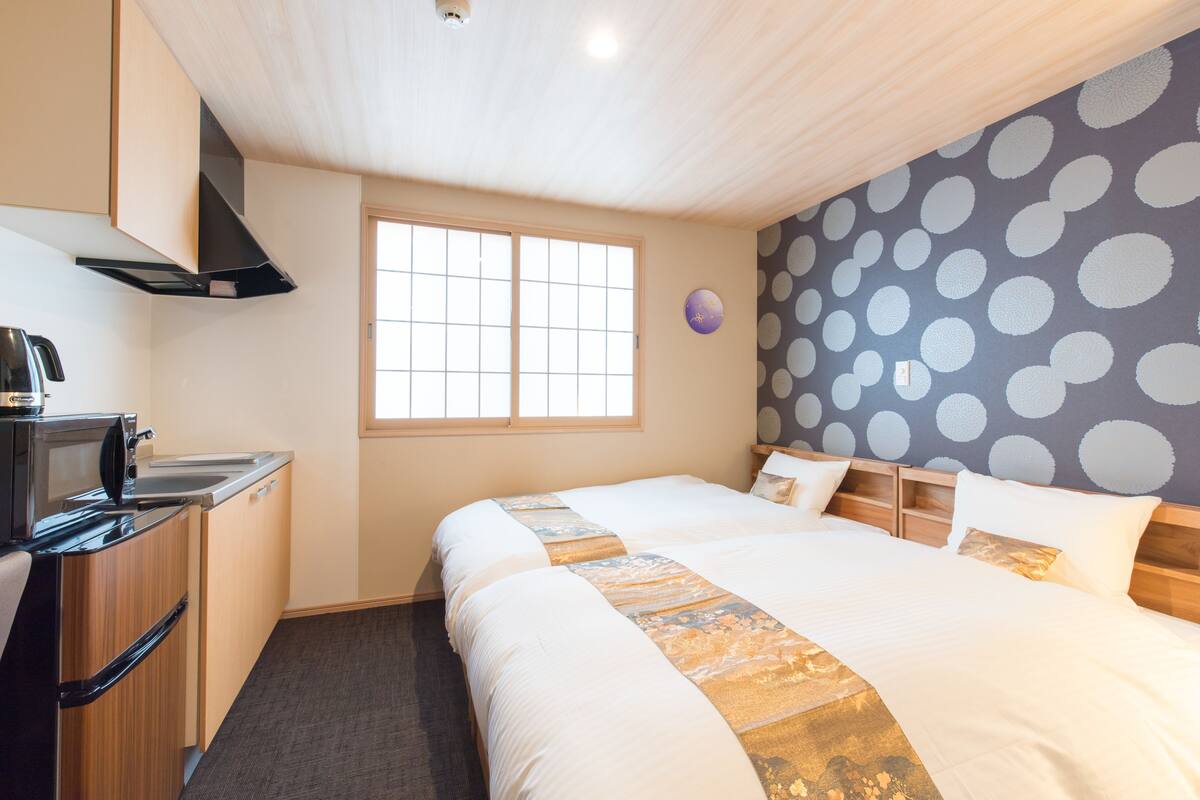 A hotel room with a bed, a window, a microwave, and a kitchenette.