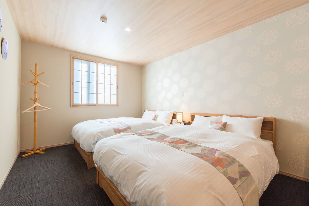 A hotel room with two beds, a window, and a wooden ceiling.