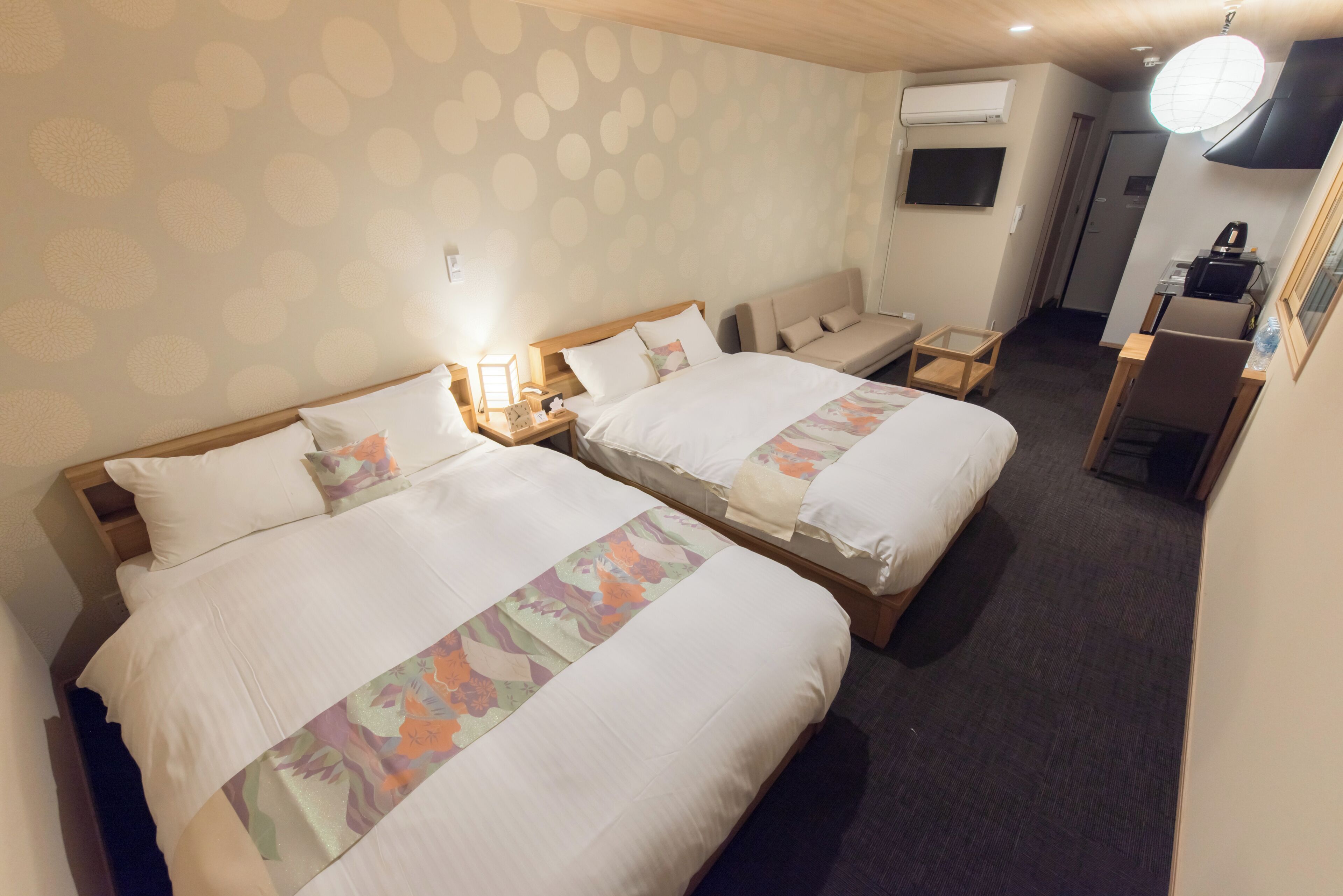 Quarto de hotel com duas camas, uma escrivaninha, uma cadeira, uma televisão e um aparelho de ar condicionado.