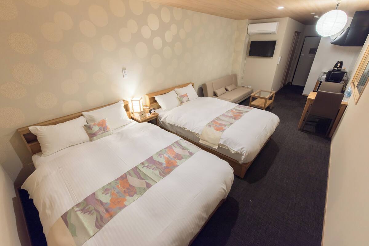 A hotel room with two beds, a desk, a chair, a TV, and an air conditioning unit.