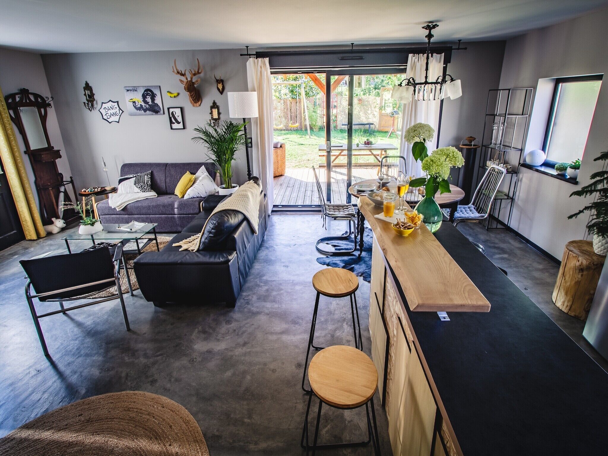 Un salon moderne avec un canapé, une table basse et un coin bar. Les murs sont décorés et il y a une vue sur l’extérieur.