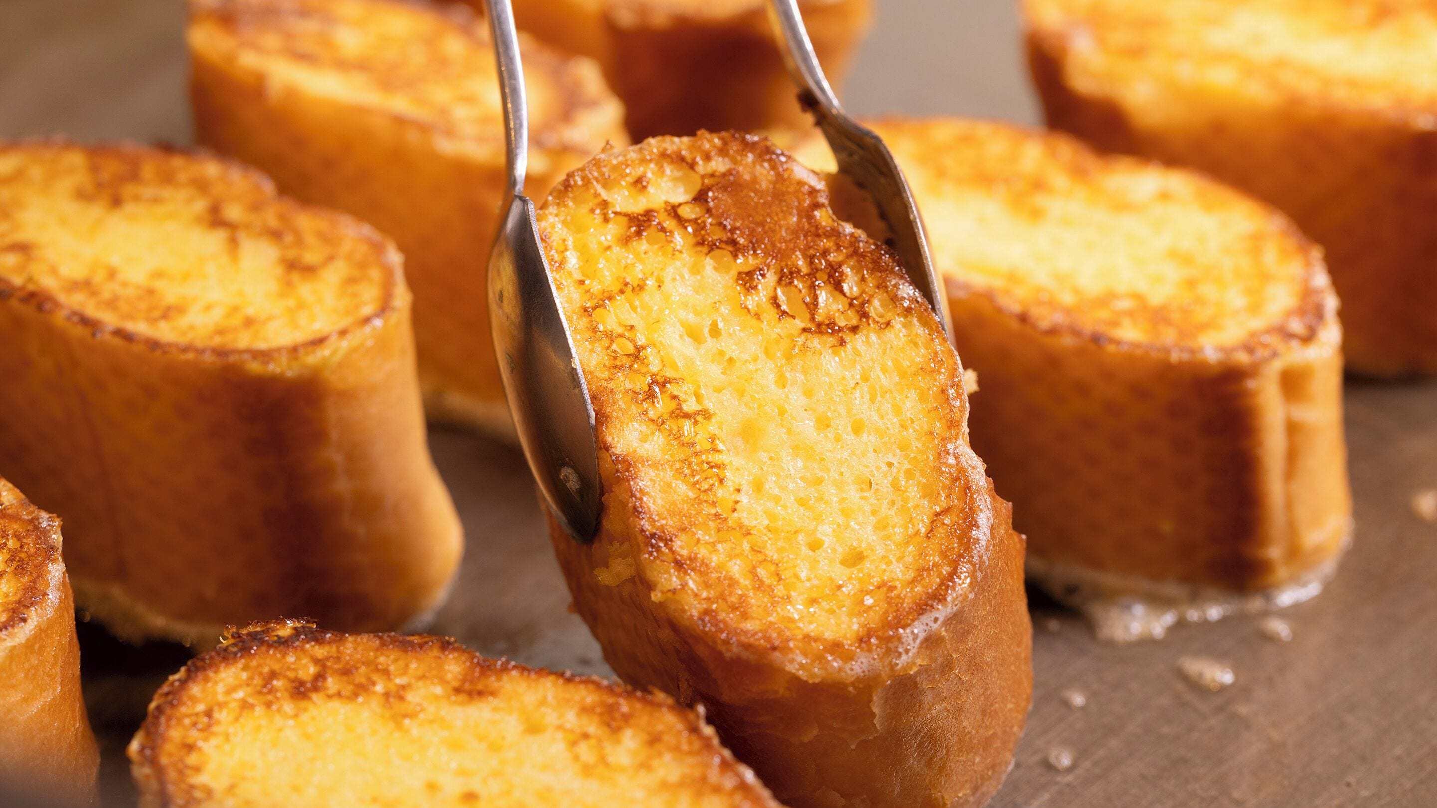 A close-up of a golden-brown baked item, possibly a cake or bread, being lifted with tongs.
