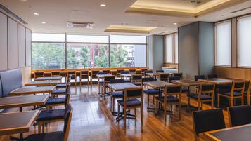 A spacious dining area with wooden tables and chairs, large windows offering a view of the city, and a modern ceiling design.