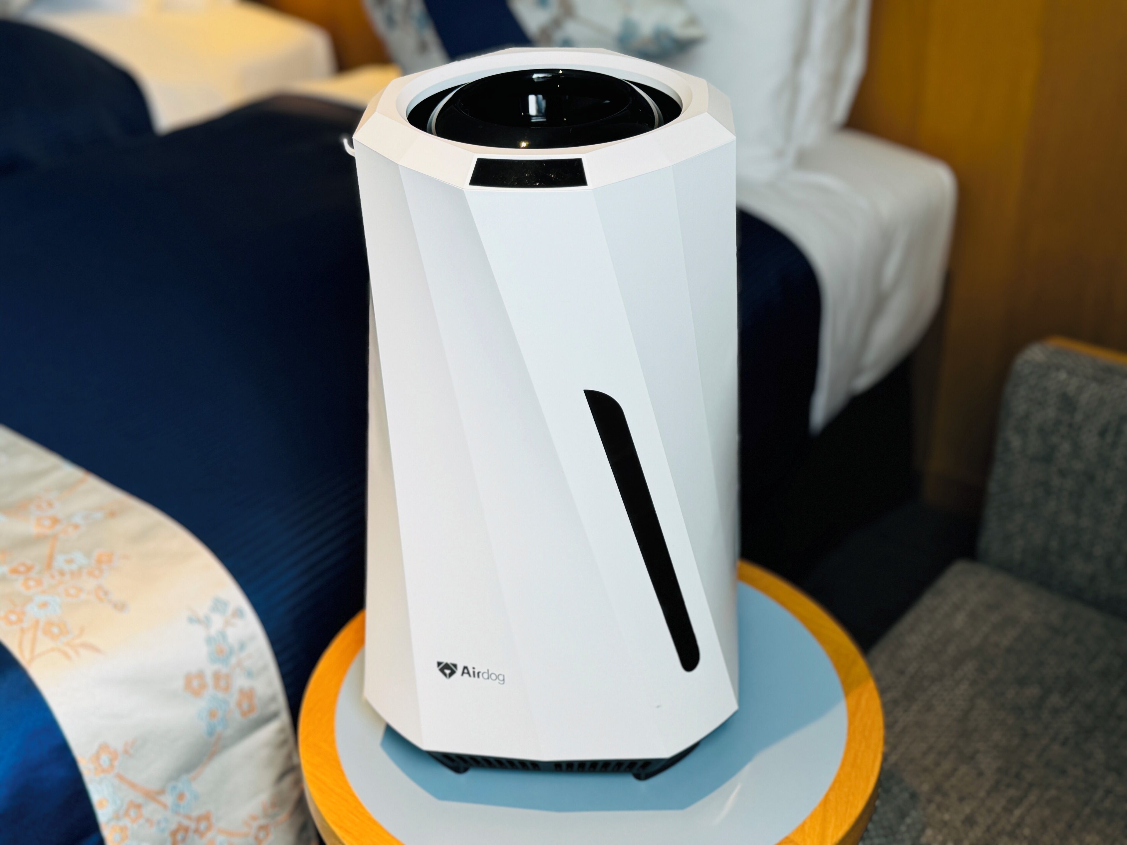 A white air purifier with the AirDog logo on a round table in a hotel room.