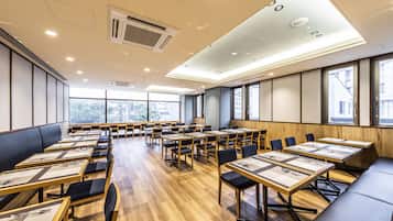 A conference room with multiple tables and chairs, large windows, and a high ceiling with recessed lighting.