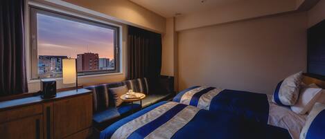 Habitación de hotel con un ventanal grande, cama, sofá, escritorio y lámpara.