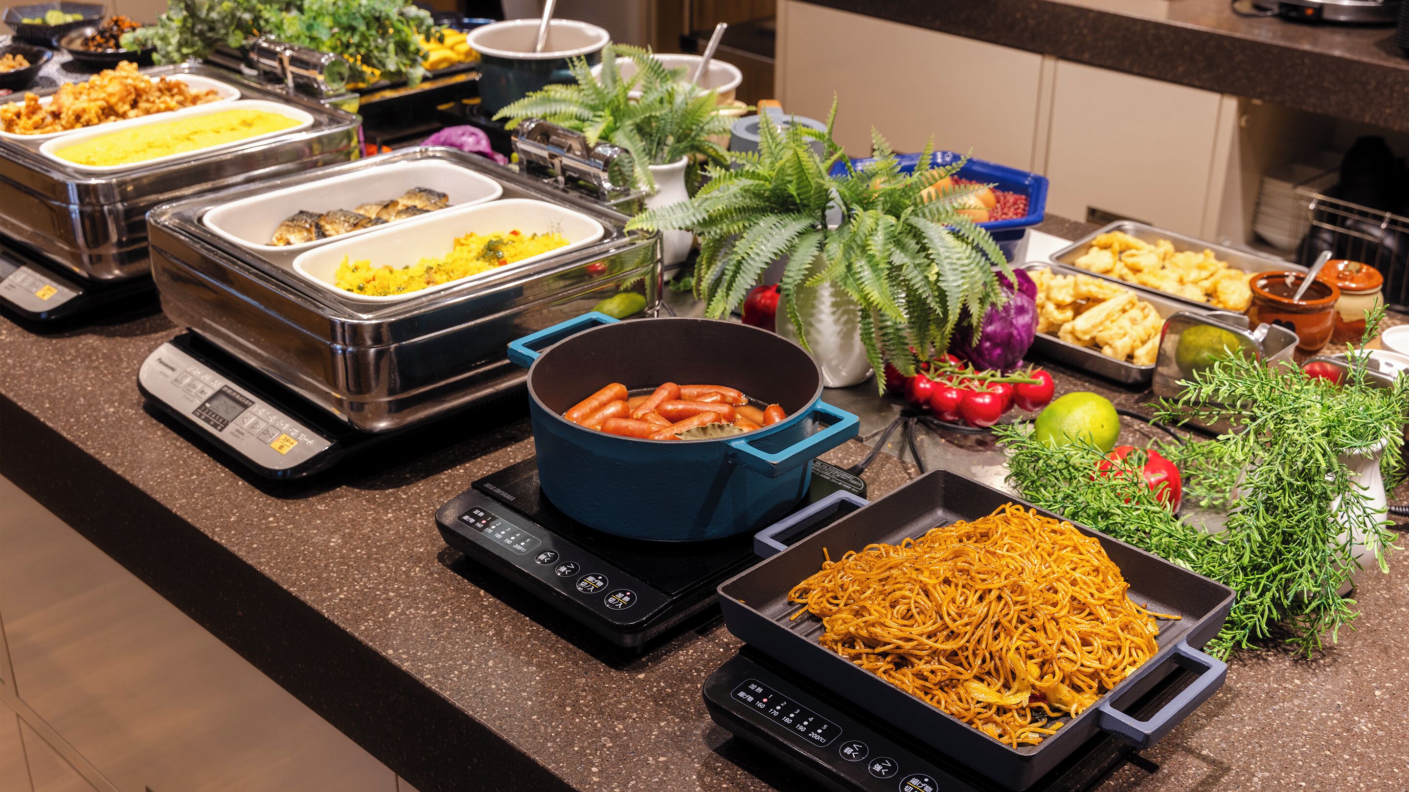 A buffet with various dishes, including a pot of carrots, a tray of noodles, and multiple containers of food.