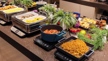 A buffet with various dishes, including a pot of carrots, a tray of noodles, and multiple containers of food.