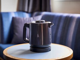 A black electric kettle on a wooden coaster on a round table.