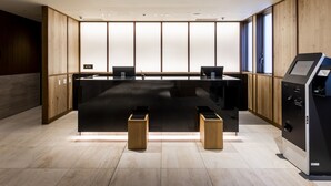 A modern reception area with a black reception desk, two wooden stools, a self-service kiosk, and a large window providing natural light. - HOTEL GRACERY Osaka Namba (Osaka)