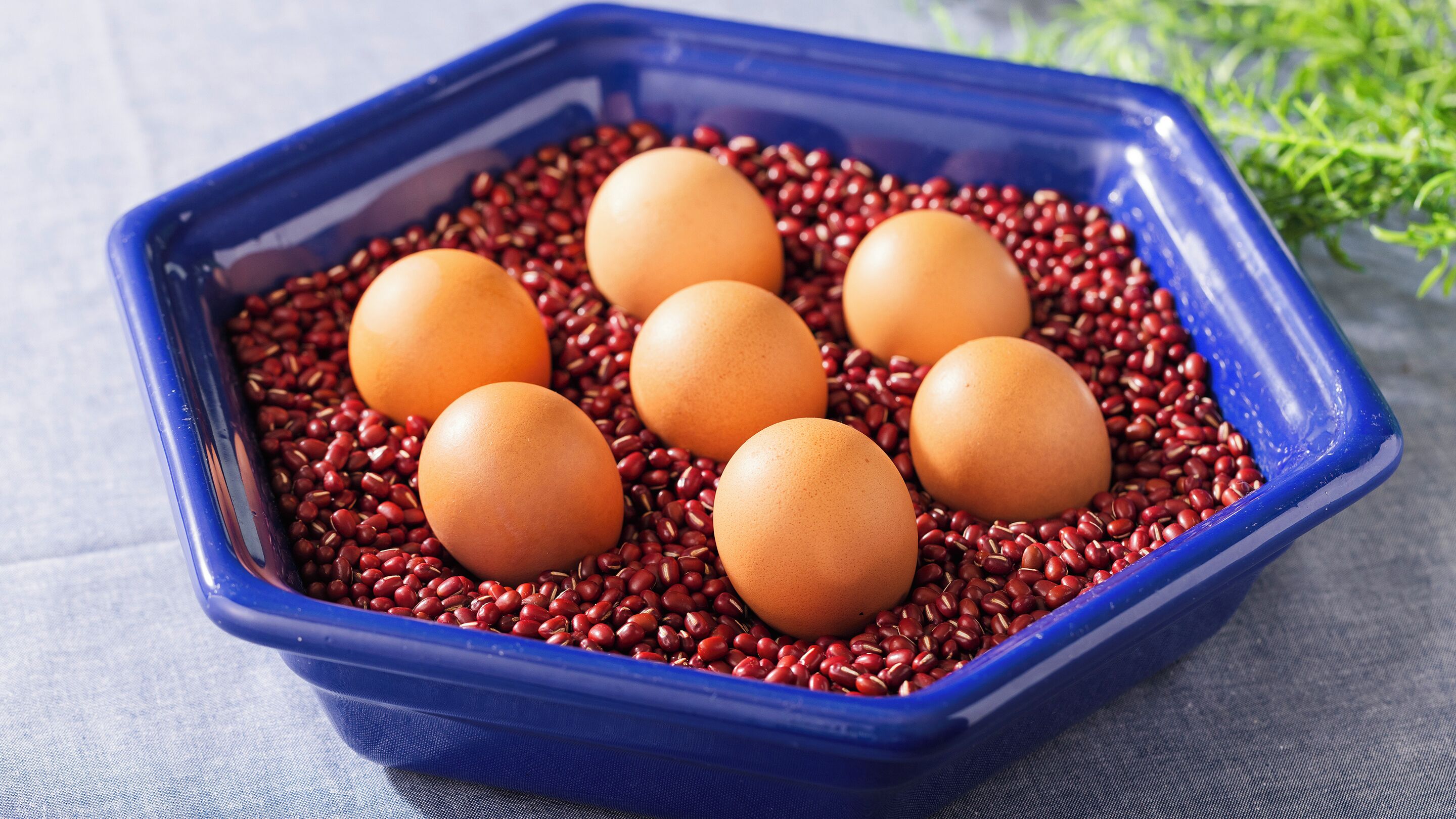 A blue tray containing six brown eggs and red beans.