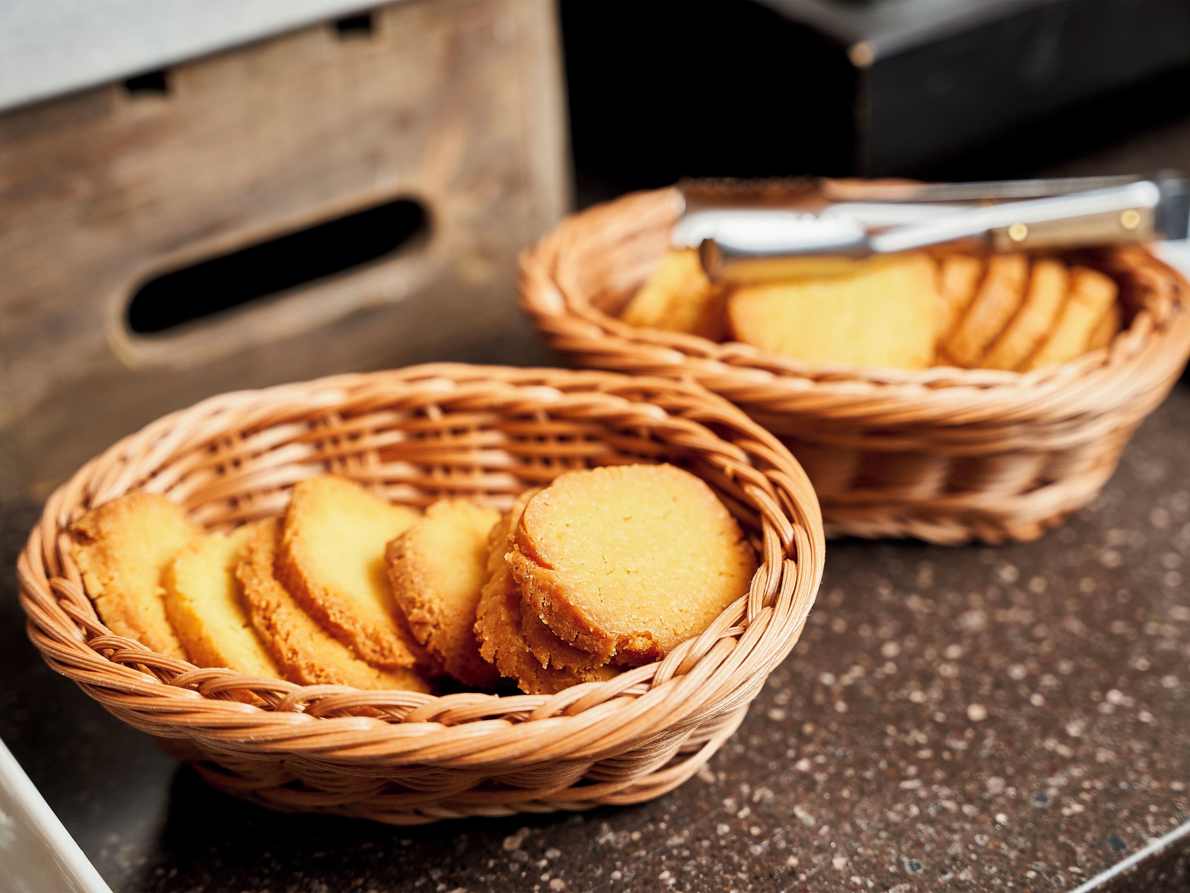 Two wicker baskets filled with round, golden-brown cookies on a dark countertop.