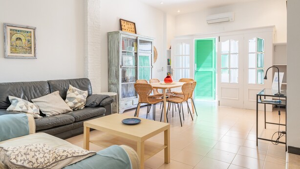 Ein Wohnzimmer mit Sofa, Couchtisch, Esstisch mit Stühlen, Schrank und einer Tür mit grünen Fensterläden.