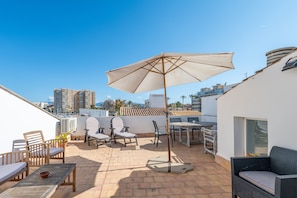 Une terrasse sur le toit, avec des sièges d’extérieur, une table et un grand parasol.