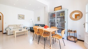 Ein Wohnzimmer mit einer Couch, einem Esstisch mit Stühlen, einem Bücherregal und einem Spiegel an der Wand.