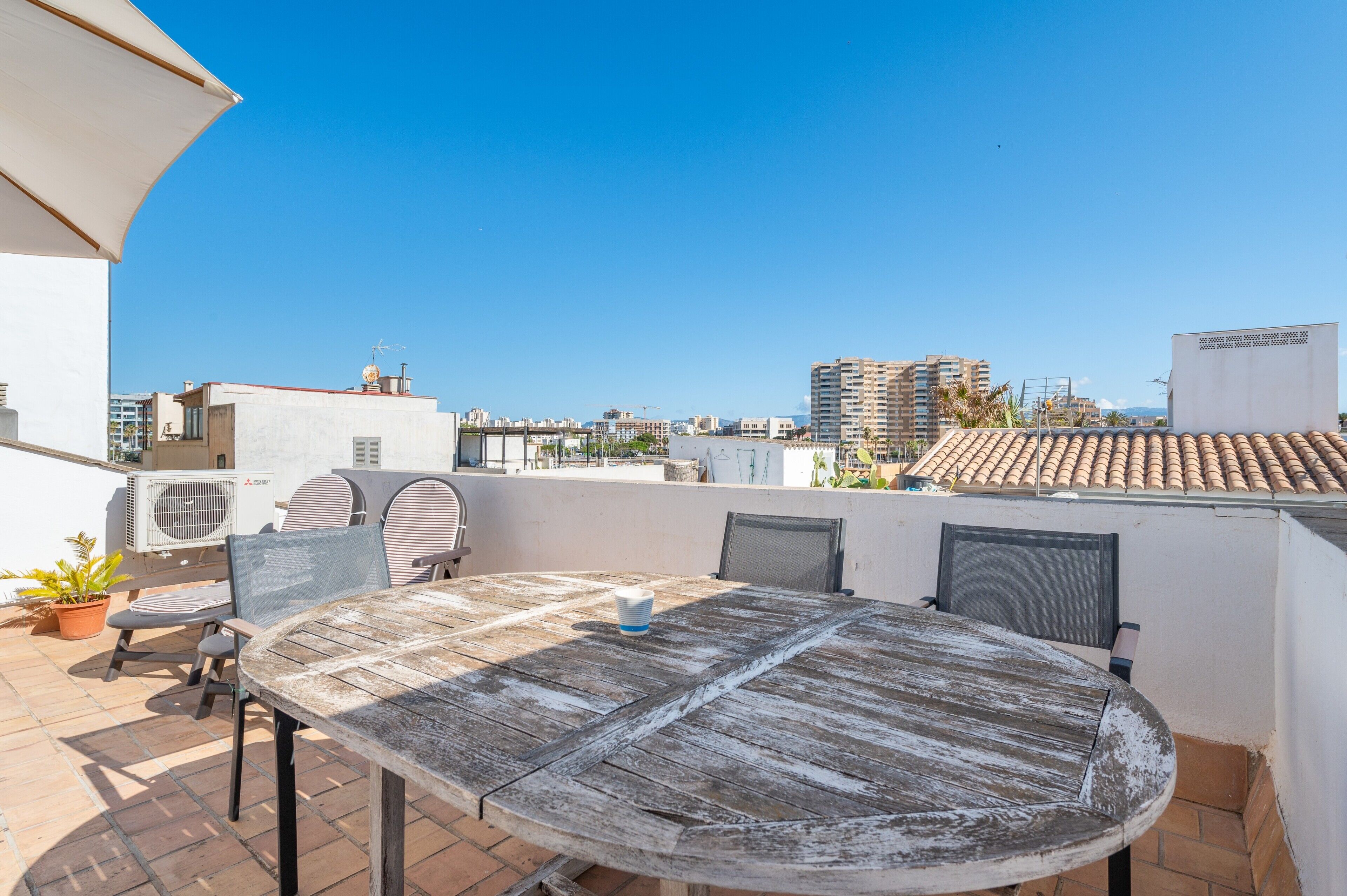 Une terrasse extérieure avec une table ronde et des chaises, des unités de climatisation et une vue sur le paysage urbain.