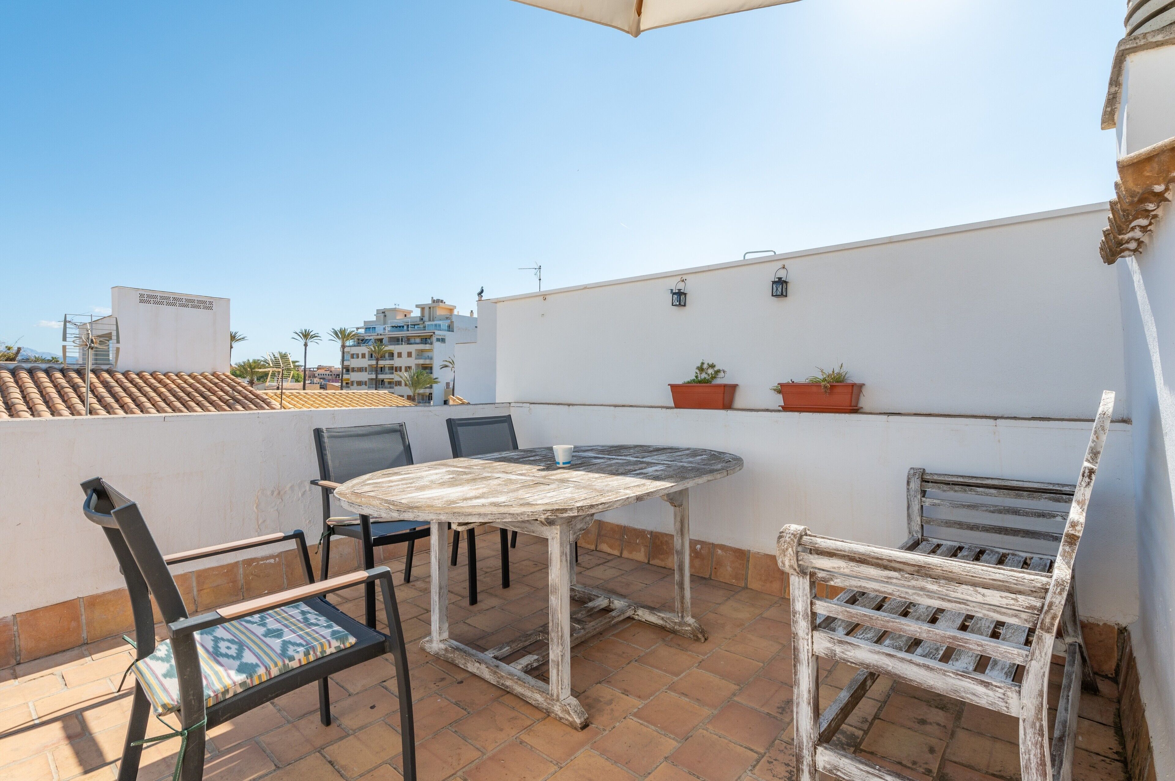 A rooftop terrace with a table and chairs, potted plants, and a view of buildings.