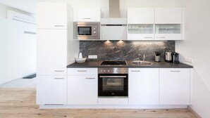 A modern kitchen with white cabinetry, a built-in oven, a microwave, and a stainless steel sink.
