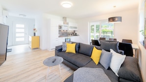 A modern living room with a grey sofa, yellow and white cushions, a small round table, and a kitchen in the background.