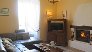 A living room with a sofa, a television, a fireplace, and a coffee table with cups and a teapot. - Holiday house near the beaches (Penmarch)