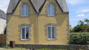 A two-story house with a yellow facade, stone accents, and a grey roof. - Holiday house near the beaches (Penmarch)