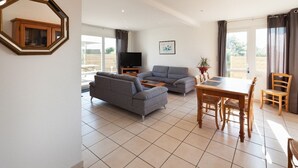 A living room with a sofa, a television, a dining table with chairs, and a potted plant.