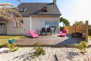 A house with a deck, two pink sun loungers, a table, and chairs.