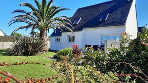 A house with a dark roof, white walls, and a well-maintained garden with a palm tree and various shrubs.