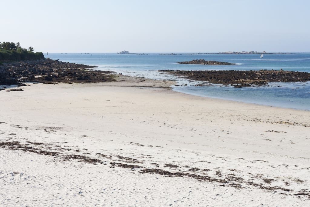 Ein Strand mit sandigem Ufer, Felsen und einem entfernten Segelboot.