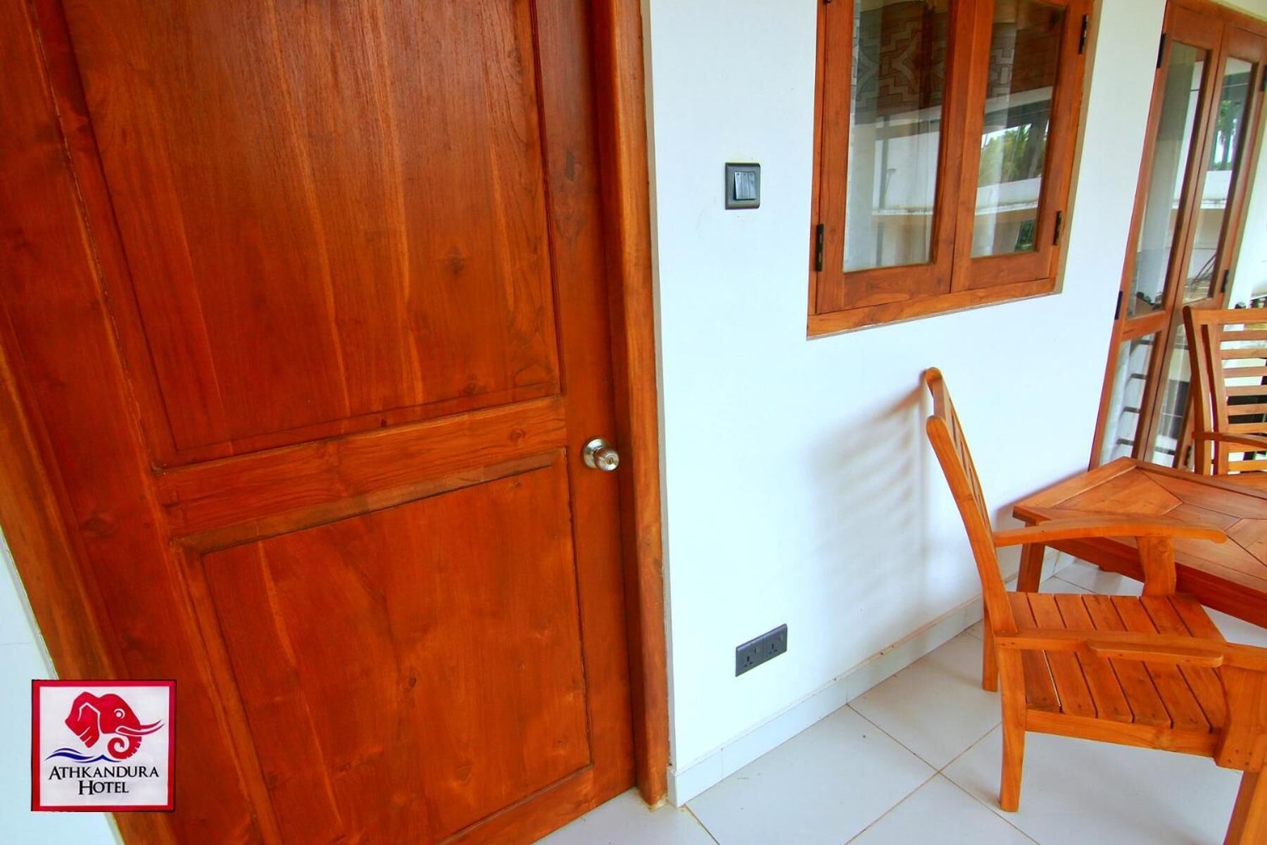 A wooden door with a window above it, a wooden table with chairs, and a logo for Athkandura Hotel.