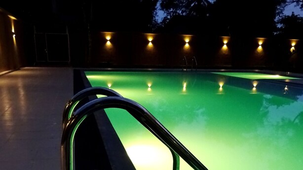 Une piscine illuminée de vert la nuit, avec un bord lumineux et une rambarde de sécurité en métal.