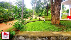 Un jardin luxuriant, avec un mur de pierre, un sentier et une chaise rouge devant un bâtiment.