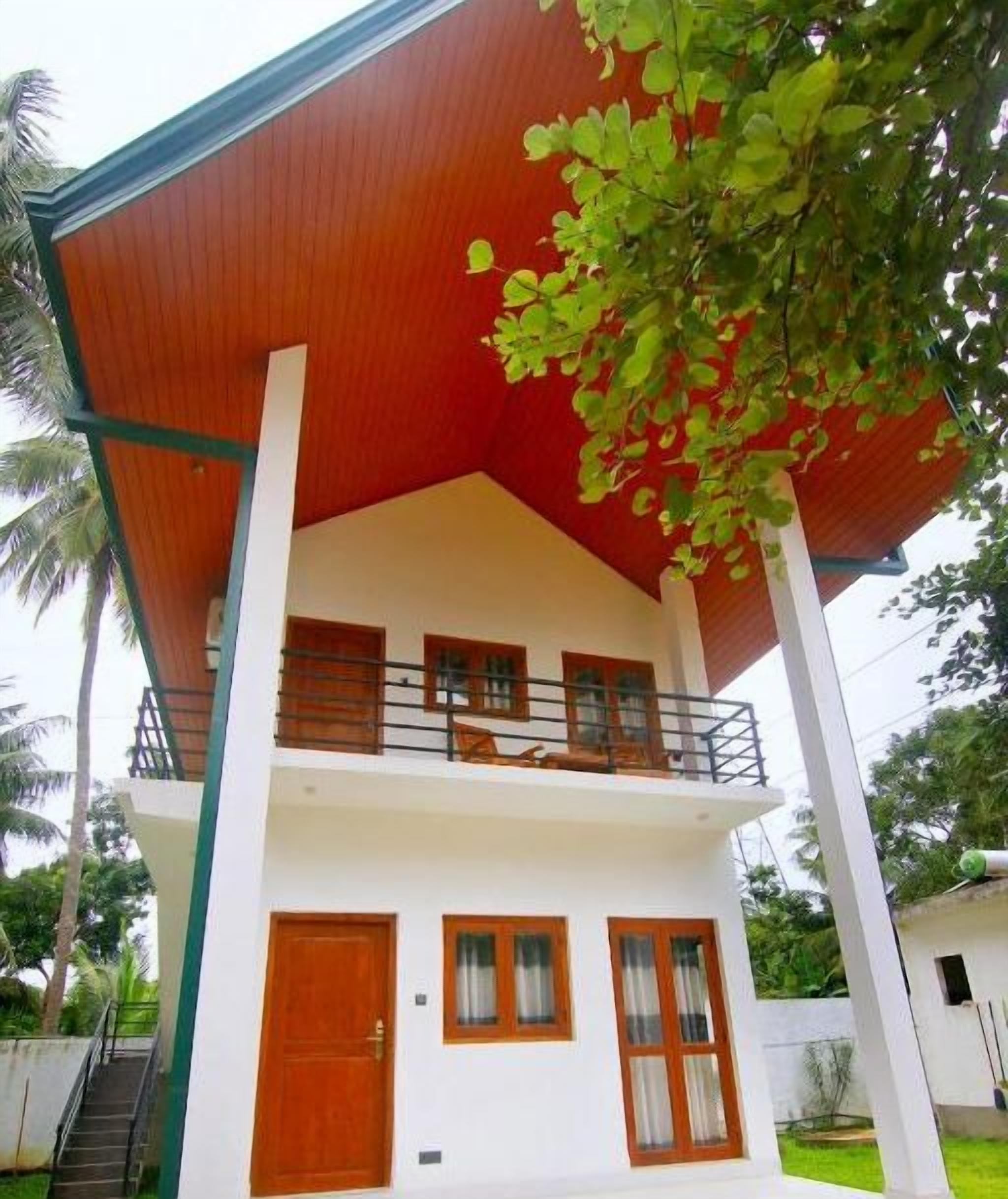 A two-story building with a red roof, white walls, and a balcony with wooden railings.