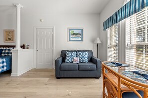 A room with a grey sofa, a framed picture on the wall, a white door, and a window with blinds.