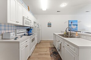 A compact kitchen with white cabinetry, a microwave, a stove, and a sink.
